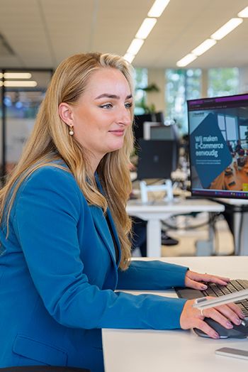 Medewerker in een blauwe blazer werkt aan een computer, met op het scherm de tekst 'Wij maken e-commerce eenvoudig', gerelateerd aan het Digitaal Product Paspoort.